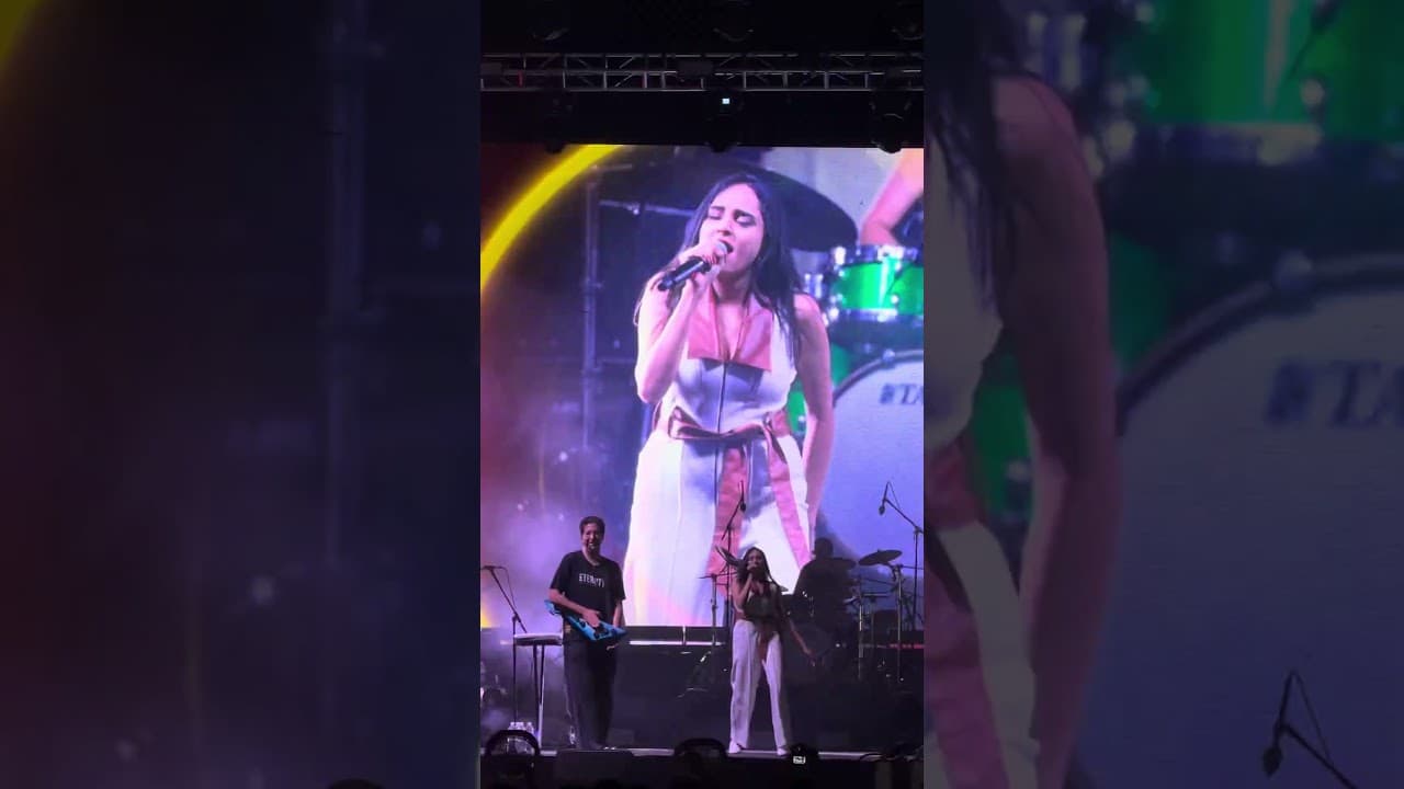 Kavya Limaye singing on a concert stage, shown on the big screen behind her